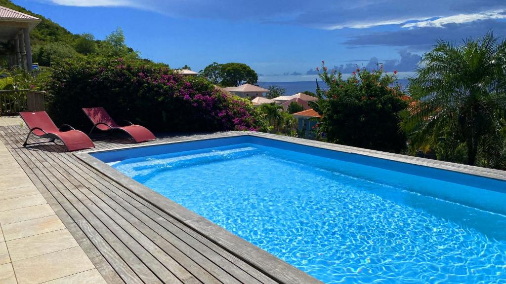 uma piscina com duas cadeiras ao lado de uma casa em Villa de charme avec piscine et magnifique vue mer em Les Anses-dʼArlets