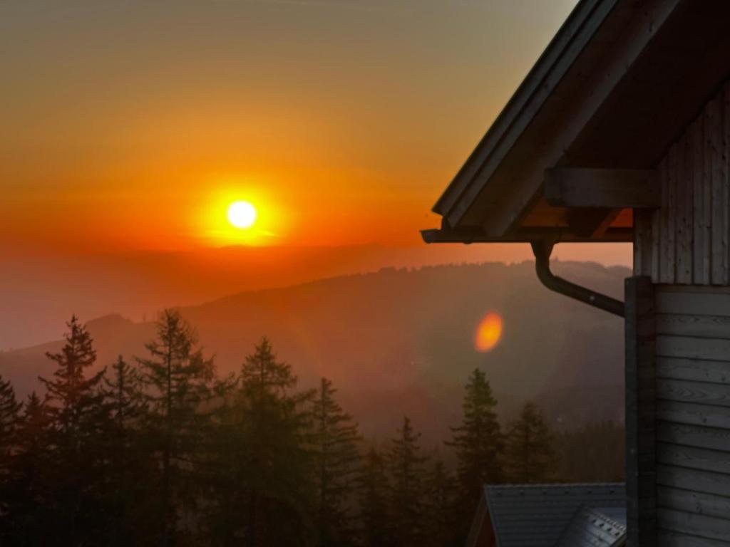 a sunrise from a house with the sun in the sky at Almhütte mit Sonnenterrasse - Holzofen - Sauna in Bad Sankt Leonhard im Lavanttal