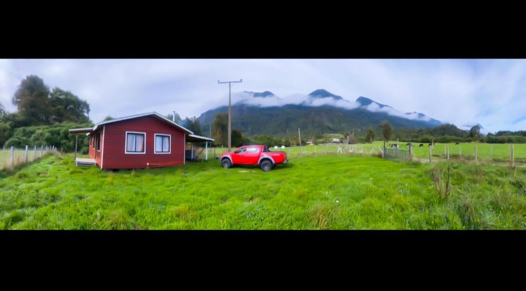 a red car parked in a field next to a house at Acogedora Cabaña in Riñinahue