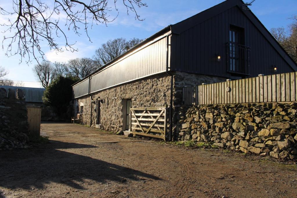 a stone barn with a stone wall and a fence at Peibio at Llanfair Hall in Dwyran