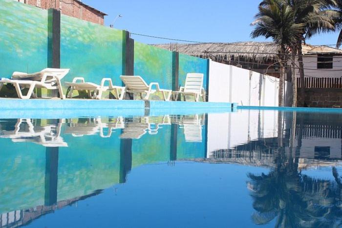 a swimming pool with white chairs and a palm tree at Ángeles del Mar in Piura