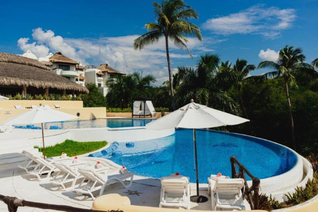 Una piscina en un resort con sillas blancas y sombrillas. en Quinta Real Huatulco, en Santa Cruz Huatulco