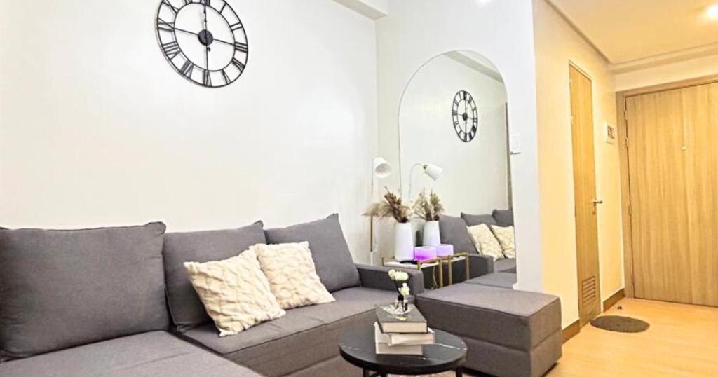 a living room with a gray couch and a clock on the wall at Condo in Quezon City, Trees Residences Tower 16 in Manila