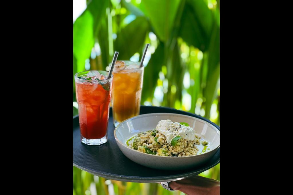 a person holding a tray with a bowl of food and two drinks at Rascals Hotel - Adults Only in Kuta Lombok