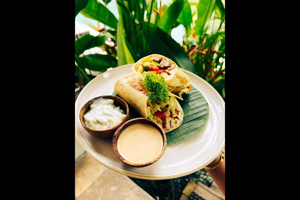 a plate with a sandwich and a bowl of dips at Rascals Hotel - Adults Only in Kuta Lombok