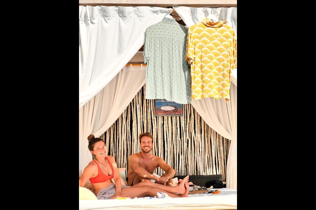 two people sitting on a bed in front of a clothes rack at Rascals Hotel - Adults Only in Kuta Lombok