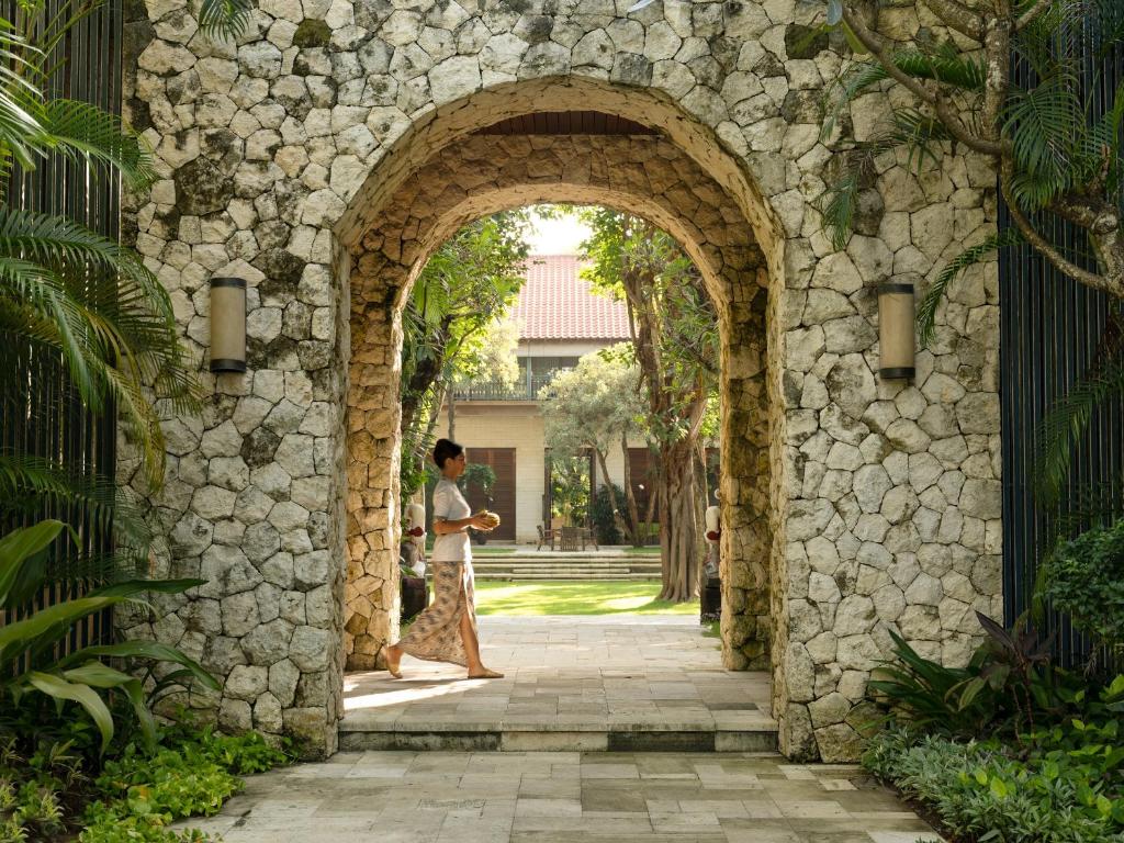 une femme qui marche à travers une arche dans un bâtiment en pierre dans l'établissement Sudamala Resort, Sanur, Bali, à anur