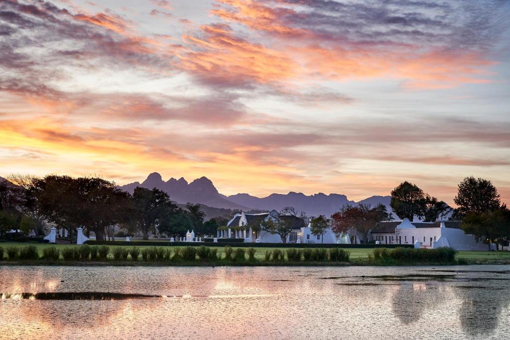 una puesta de sol sobre un lago con casas y montañas en Vergenoegd Löw Boutique Hotel & Spa en Ciudad del Cabo
