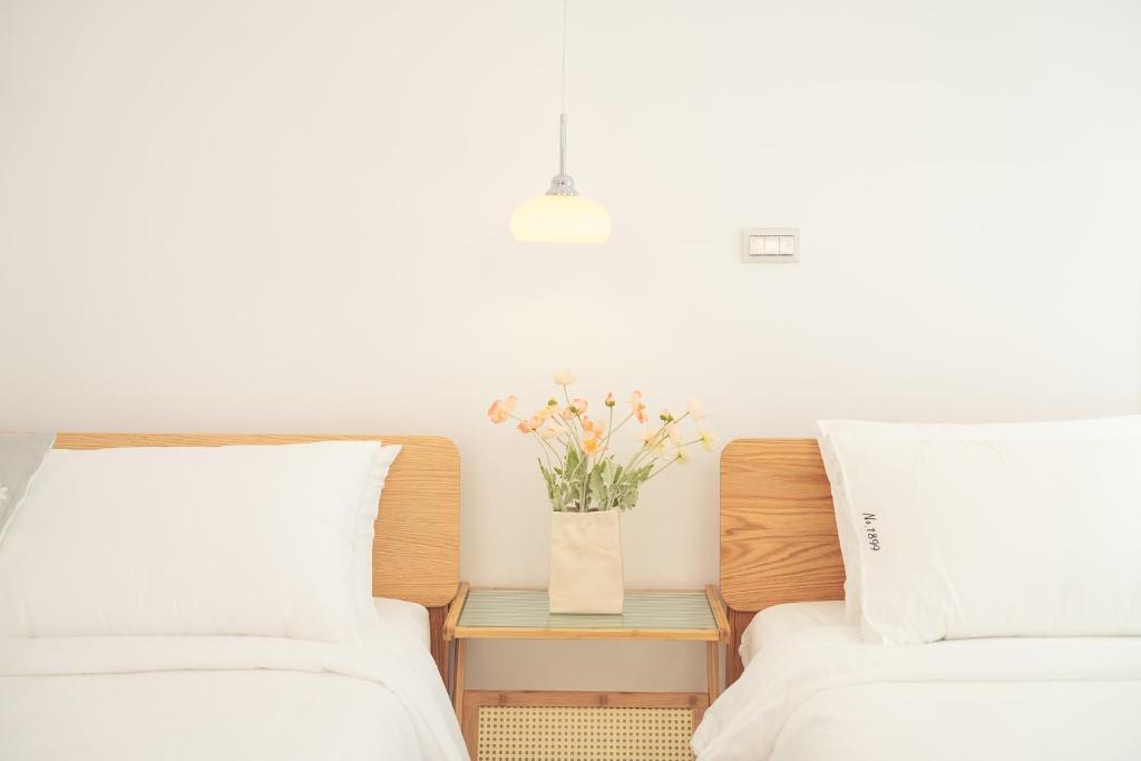 two beds with white sheets and a vase with flowers on a table at No.1899 House in Meinong