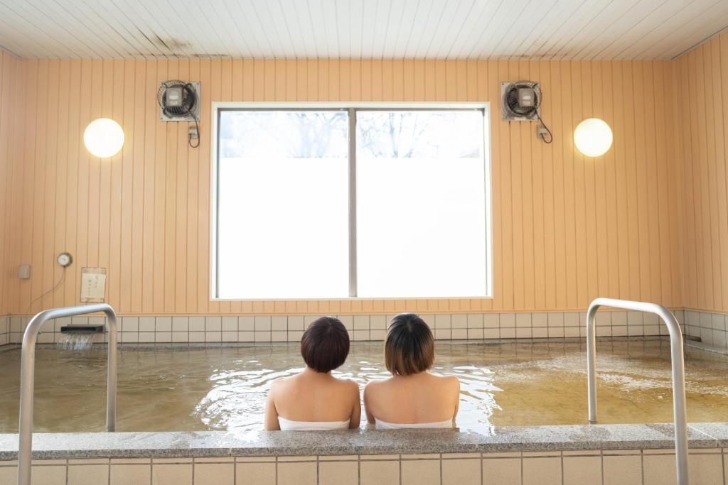 zwei Frauen sitzen in einer Badewanne mit Fenster in der Unterkunft Kobohudonoyu in Sukagawa