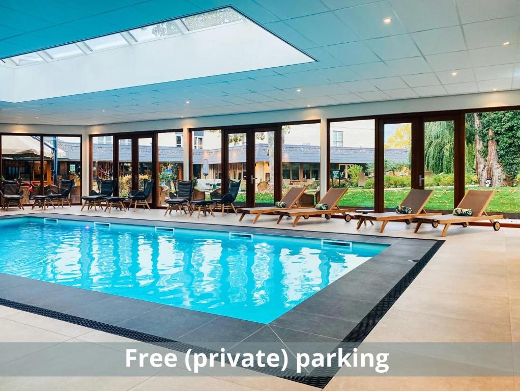 einen Pool in einem Hotel mit Liegestühlen und einer großen Glaswand in der Unterkunft Hotel Schaepkens van St Fijt in Valkenburg