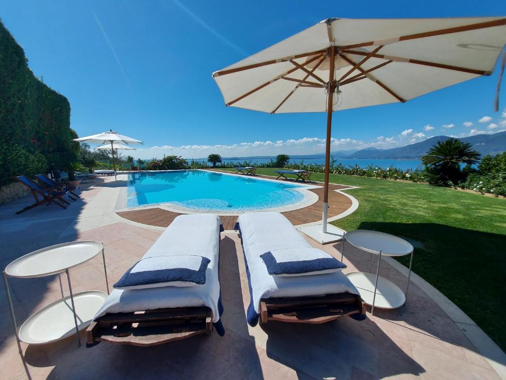 トッリ・デル・ベーナコにあるMINI DI LUSSO CON PISCINAのラウンジチェア2脚とパラソル付きのプールが備わります。