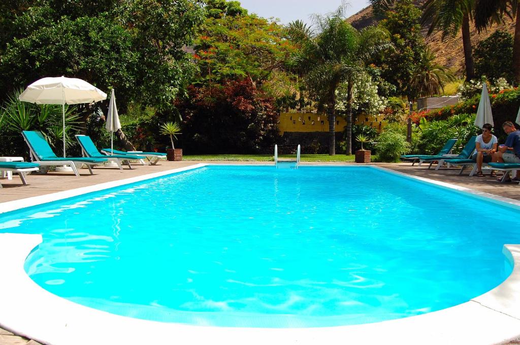 a large blue swimming pool with blue chairs and an umbrella at Finca Borbolan y La Roseta in Valle Gran Rey