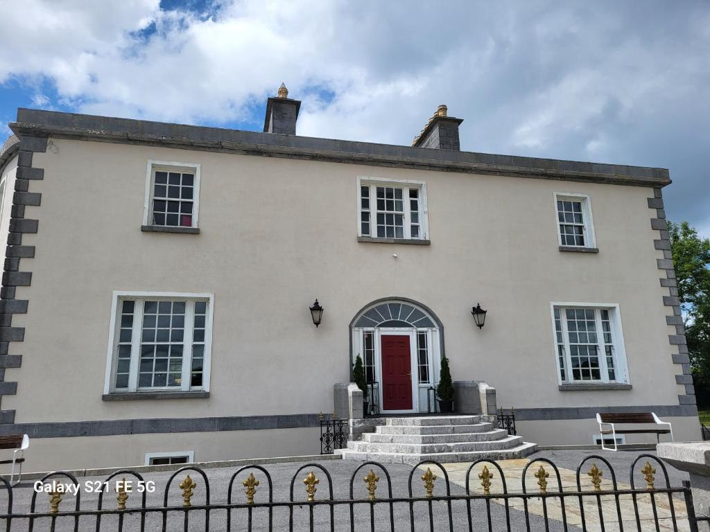 een wit huis met een rode deur en een hek bij Ballycurrin House in Galway