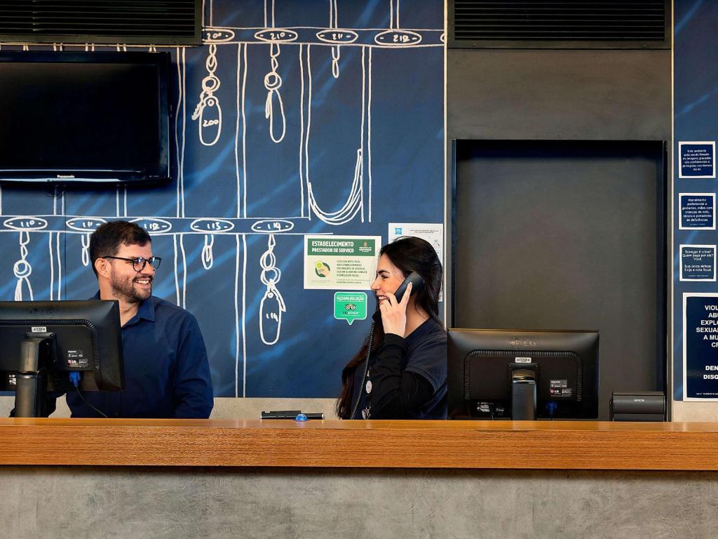 a man and a woman sitting at a counter talking on a cell phone at ibis budget Sao Paulo Paraiso in Sao Paulo