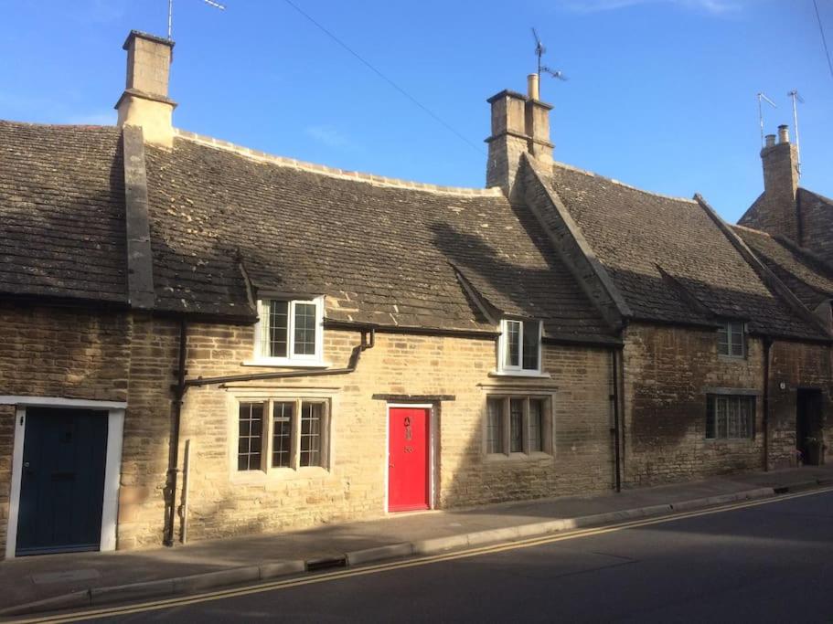 an old brick building with a red door on a street at Lovely listed cottage in old centre with garden. in Oundle