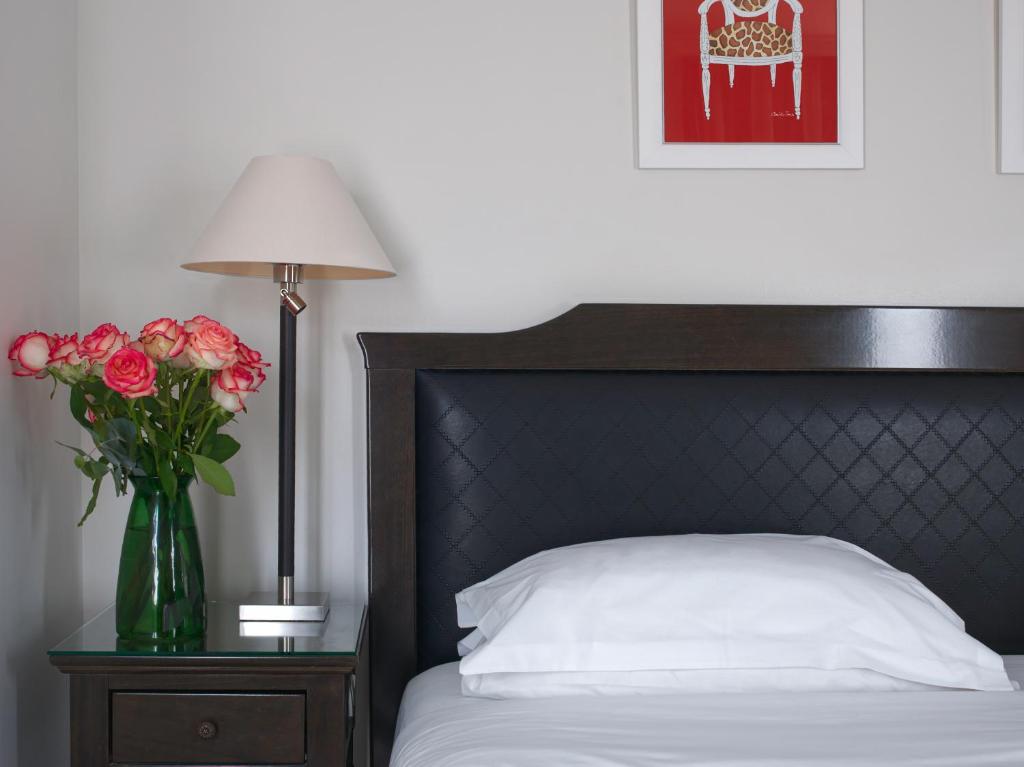 a bed with a vase of roses on a table with a lamp at Hotel Royal Saint Honore Paris Louvre in Paris