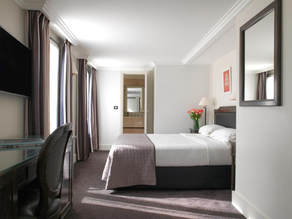 a hotel room with a bed and a desk and a mirror at Hotel Royal Saint Honore Paris Louvre in Paris