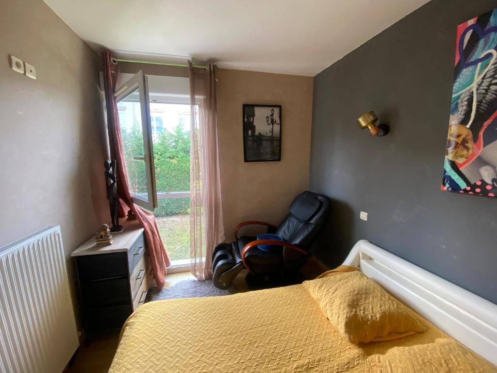 a bedroom with a bed and a chair and a window at Agréables chambres dans maison suspendue in Saint-Étienne