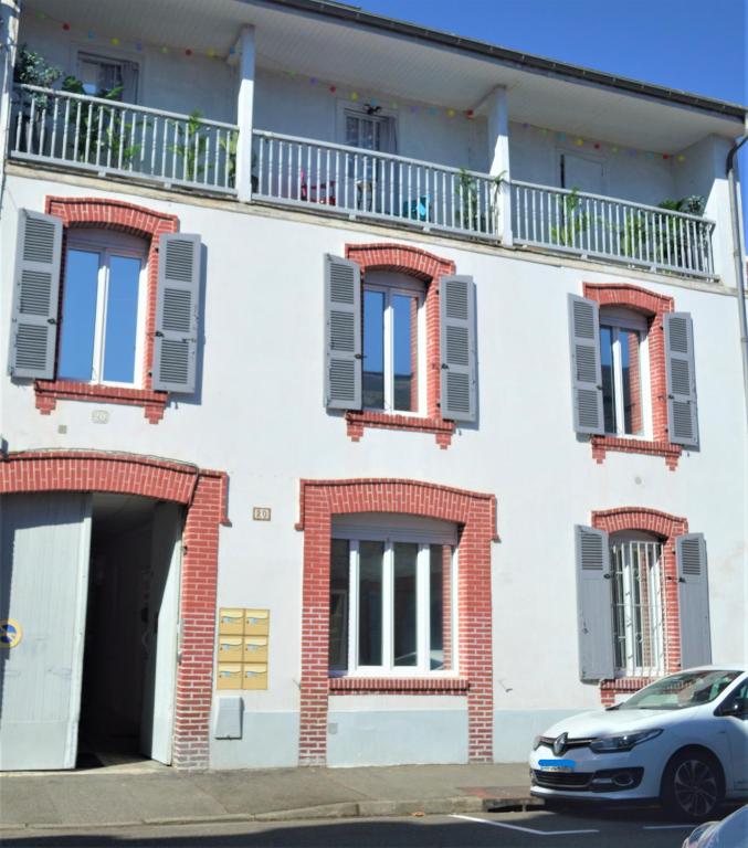 un bâtiment blanc avec des fenêtres et une voiture garée devant dans l'établissement Tarbes Immeuble résidentiel labelisé et classé Proche des Halles Marcadieu et Brauhauban et du Parc des expositions - Appartements Appaloosa T2 Rdc et Pyrénéa T2 au 1er étage avec terrasse couverte -Parking gratuit-, à Tarbes