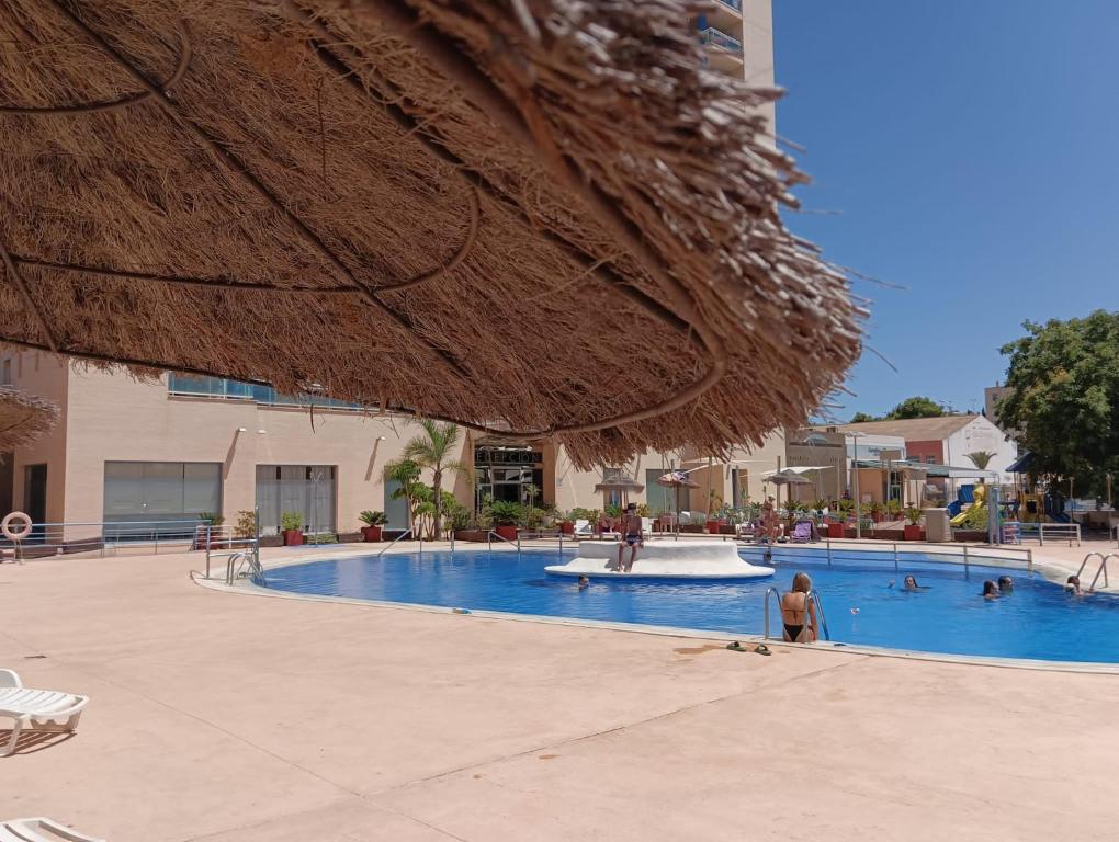 ein Schwimmbad mit einem Strohschirm und Menschen darin in der Unterkunft Sunny place. in Guardamar del Segura