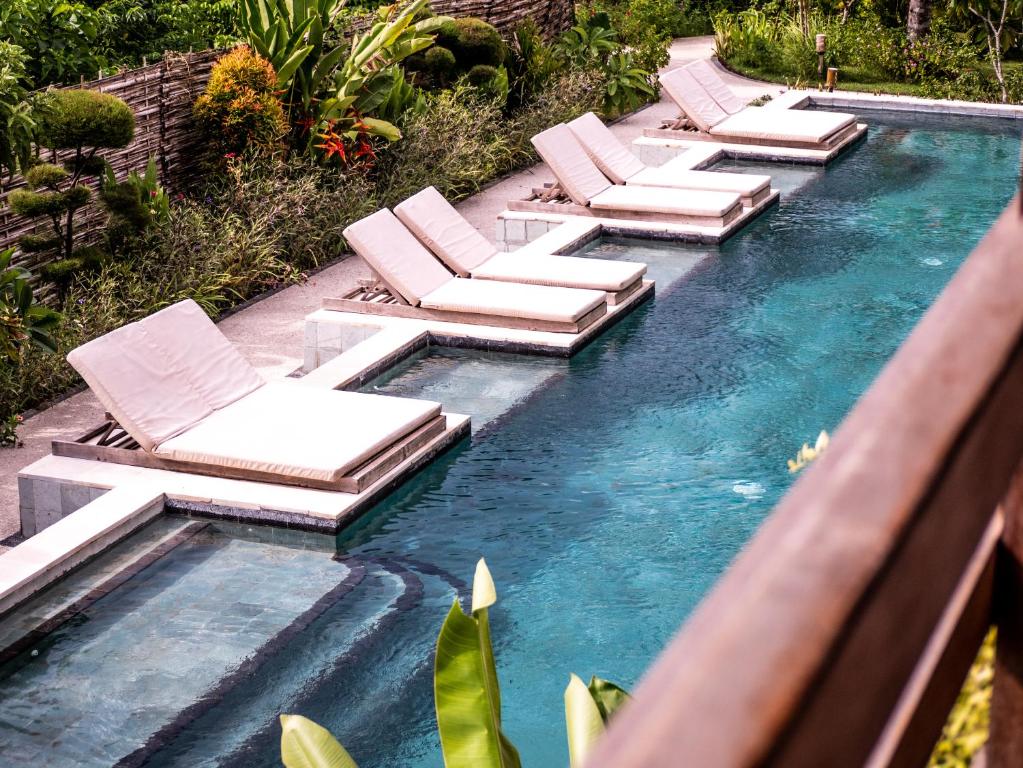 uma fila de espreguiçadeiras e cadeiras numa piscina em Mango Lodge em Selong Blanak