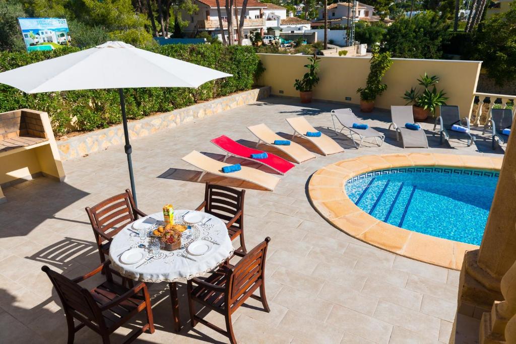 a table with chairs and an umbrella next to a pool at Villa Llobell - Plusholidays in Moraira