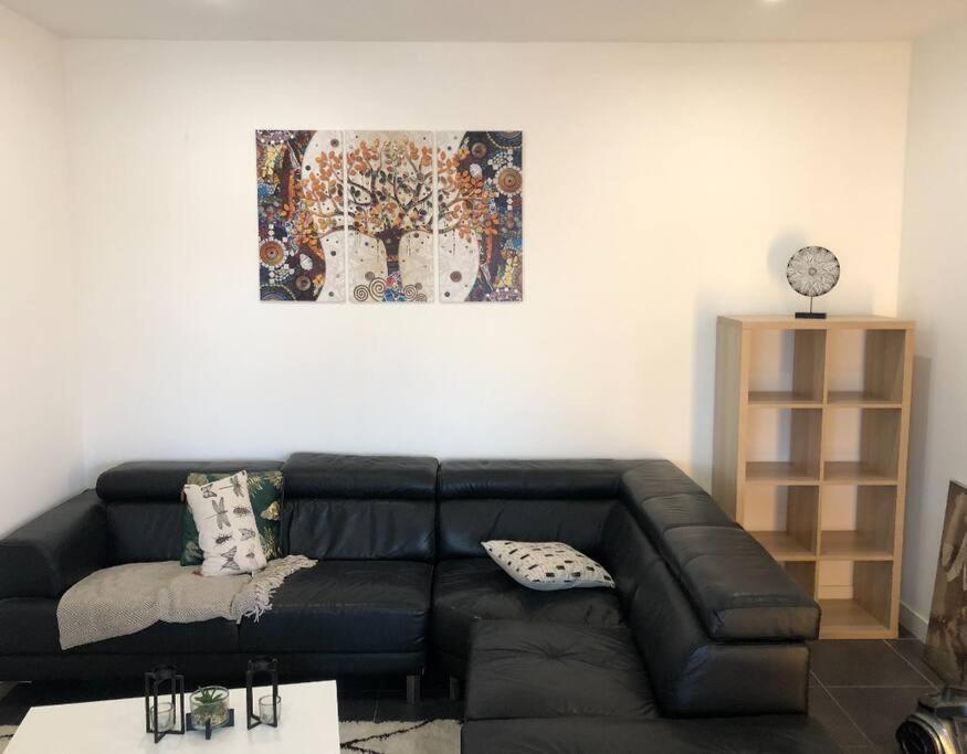 a black leather couch in a living room with a painting at Chambre qualité hôtel 4 etoiles dans un appartement partagé in Frouzins