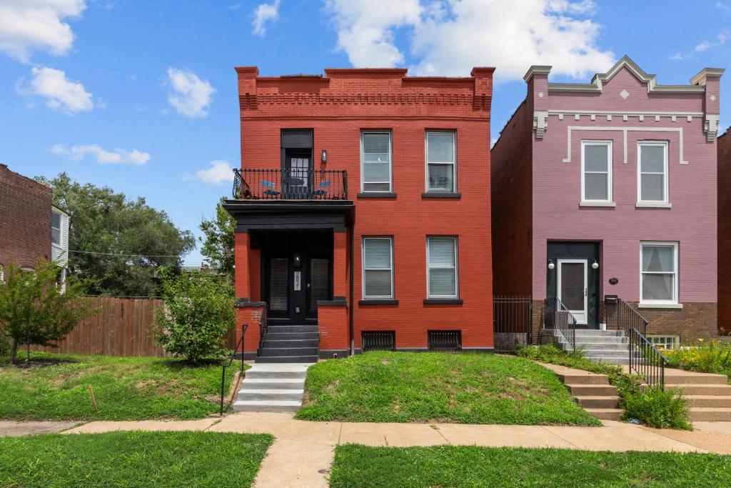 a red building with a balcony in front of two buildings at Chic 4-Bed Home near Attractions - JZ Vacation Rentals in Soulard