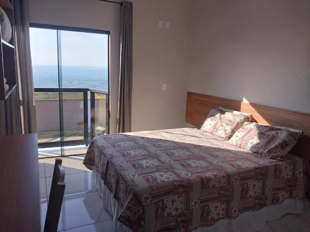 um quarto com uma cama e uma grande janela em Hotel-Pousada Quartzo Rosa em São Thomé das Letras