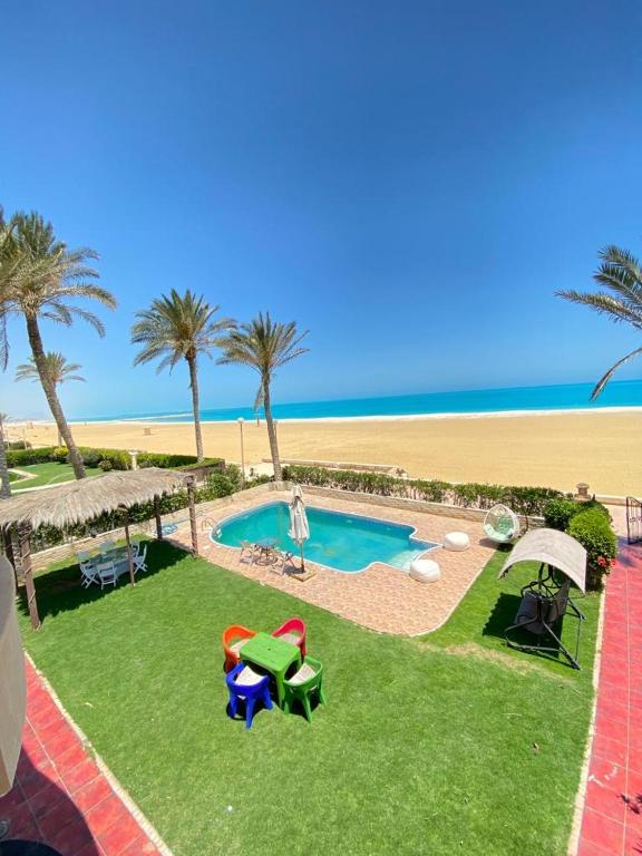 a small swimming pool with palm trees and the beach at فيلا اول صف بحر مارينا الساحل الشمالي العلمين برايفت بول in El Alamein
