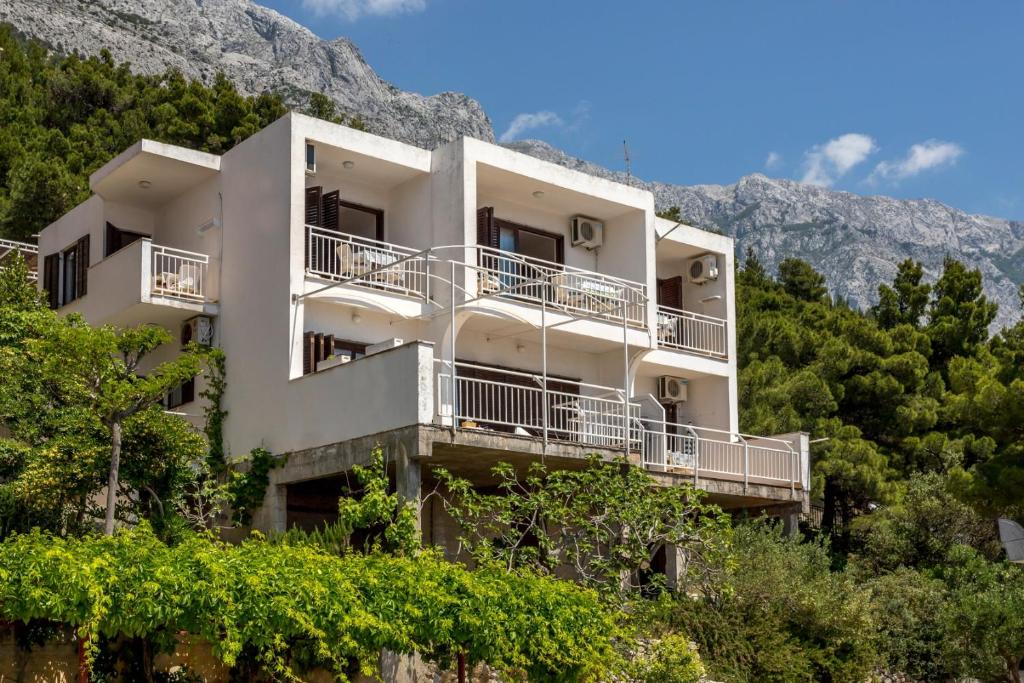 a white building with trees in front of a mountain at Apartments with parking space Baska Voda, Makarska - 301 in Baška Voda