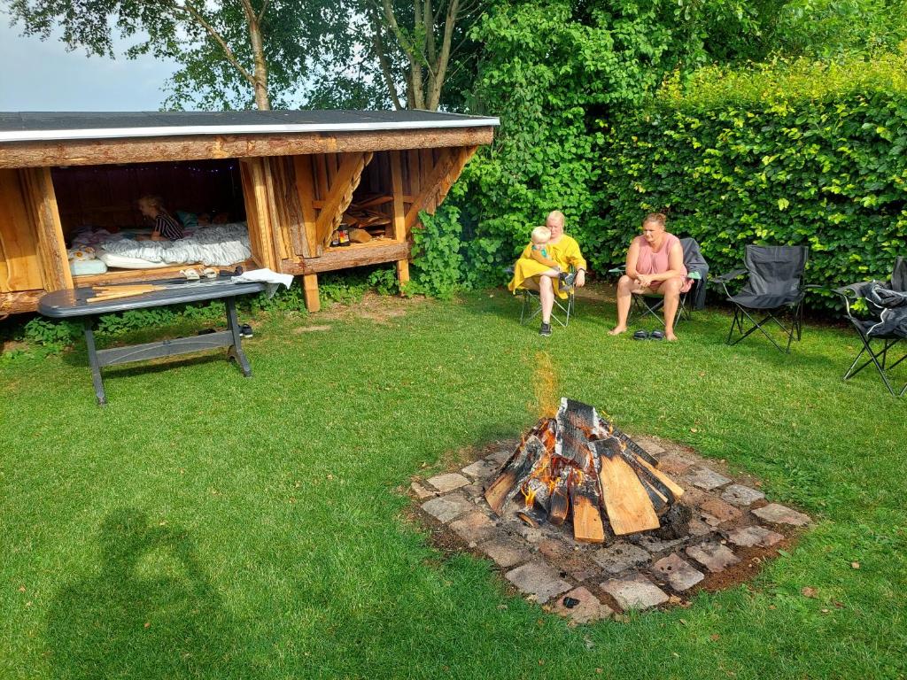 a family sitting around a fire pit in a yard at Luksus Shelter med vildmarksbad in Flemming