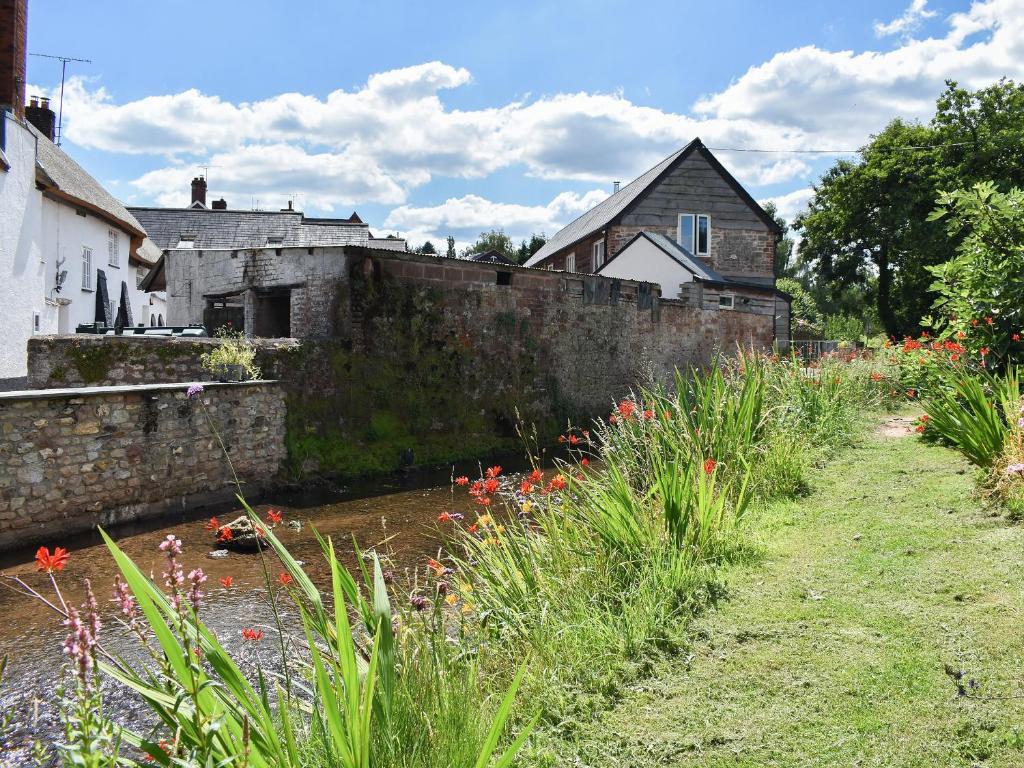 an old stone wall next to a river with flowers at Fair Maid in Kentisbeare