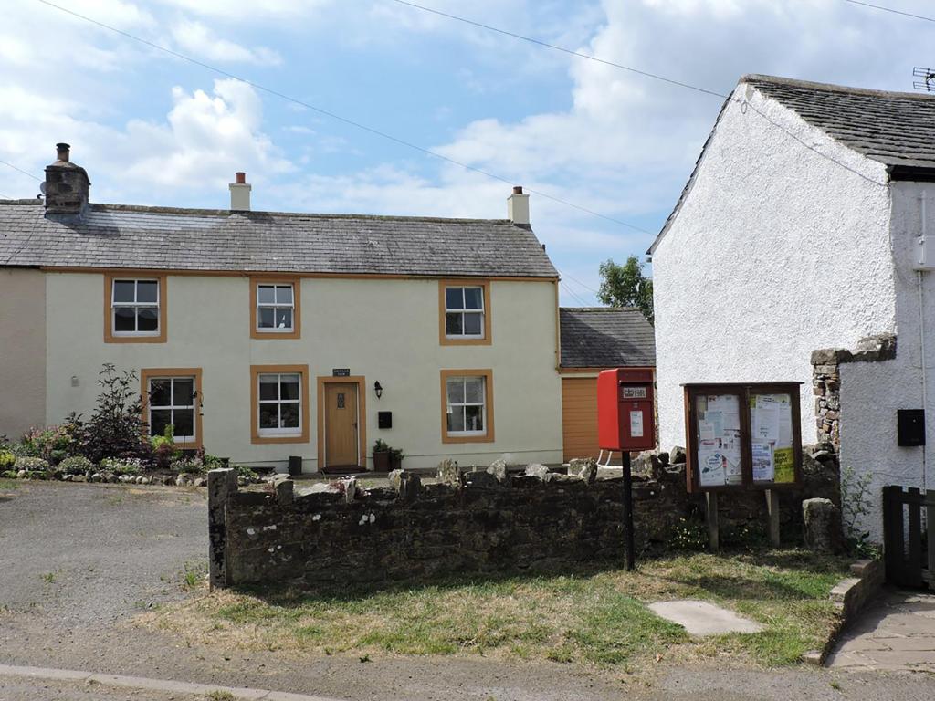 uma casa branca com uma porta vermelha e uma cerca de pedra em Greenah View em Uldale