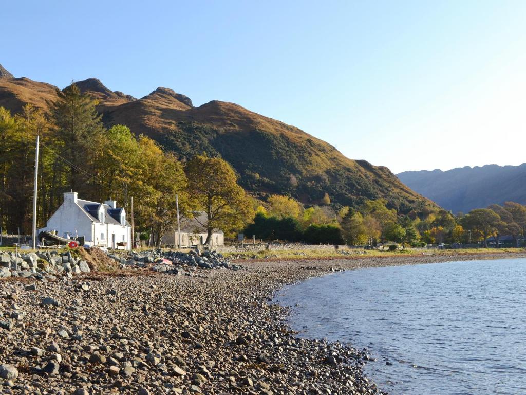 a house on a rocky beach next to the water at Shore Cottage in Arnisdale