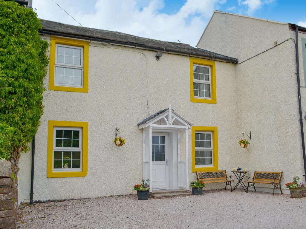 a white house with yellow windows and a patio at Bumblebee Nook in Penrith