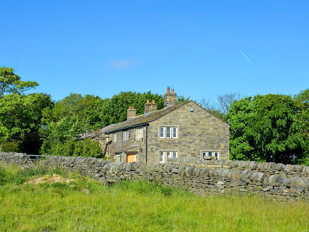 een oud stenen huis achter een stenen muur bij Higher Kirkstall Wood Farm in Ingrow