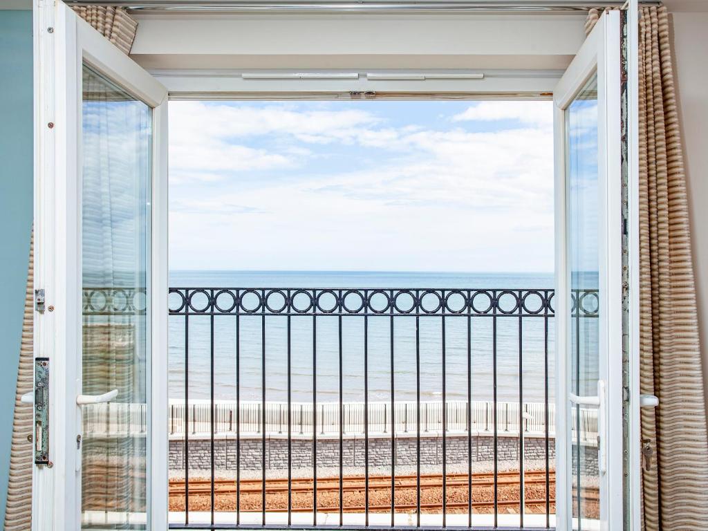 a room with a view of the beach through a sliding glass door at Waves - Great Cliff in Dawlish
