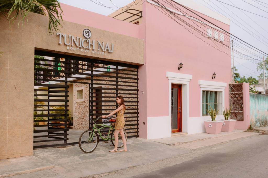 a woman walking a bike in front of a pink building at Hostal Tunich Naj & Hotel in Valladolid