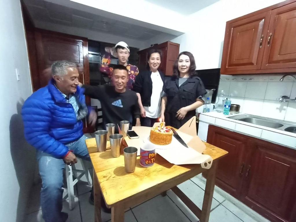 un gruppo di persone che si trovano intorno a un tavolo con una torta di Albergue Camry Backpackers佳美背包客旅馆 a Cuenca