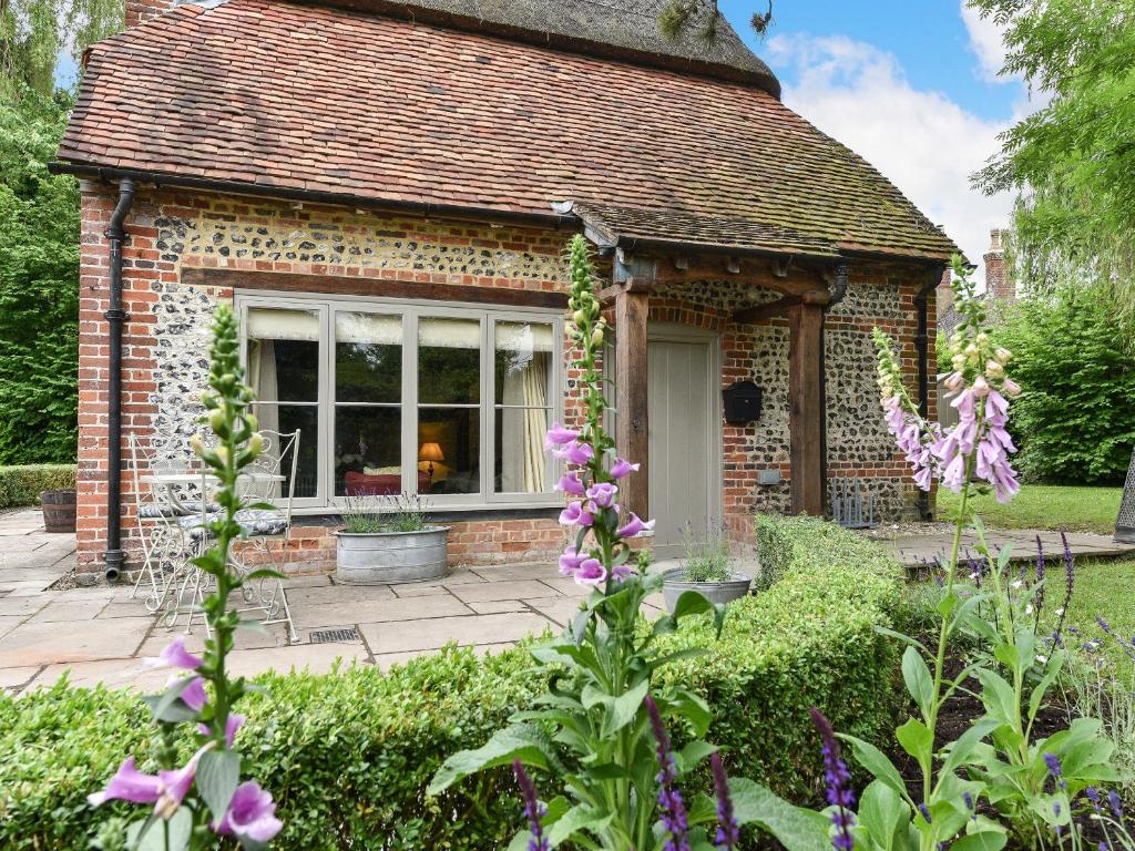 a small brick house in a garden with purple flowers at Peppercorn Cottage in Cheriton