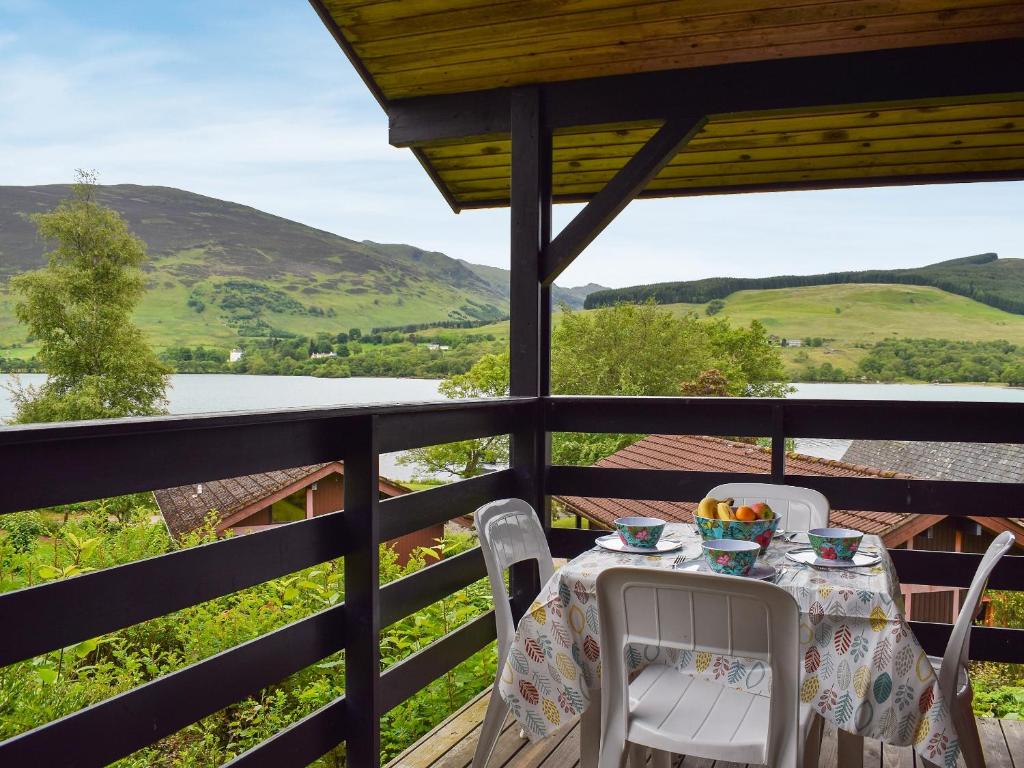 a table and chairs on a porch with a view of a lake at Loch Earn View Lodge in Lochearnhead