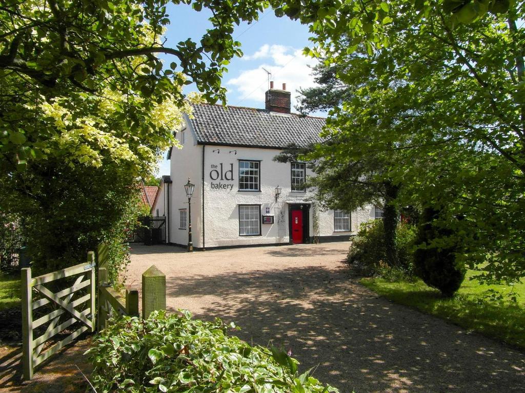 an old white building with a red door at The Old Bakery in Pulham Saint Mary Magdalene