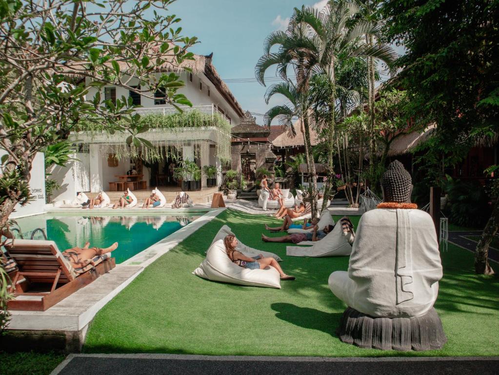 eine Gruppe von Menschen, die auf dem Rasen am Pool sitzen in der Unterkunft Puri Garden Hotel & Hostel in Ubud