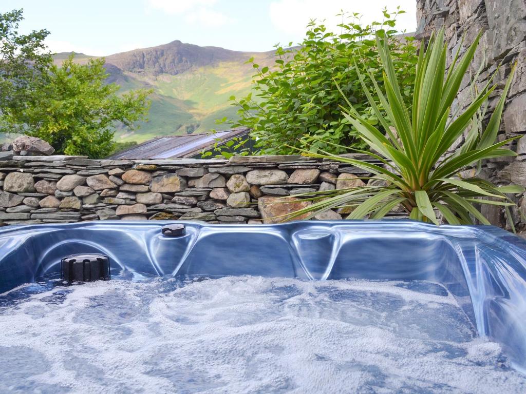 a hot tub in a backyard with a stone wall at Field House Cottage - Uk12573 in Borrowdale