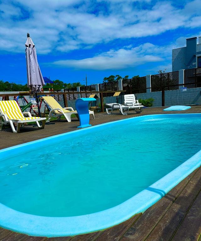 a large swimming pool with chairs and a umbrella at POUSADA ROSA e POESIA in Praia do Rosa
