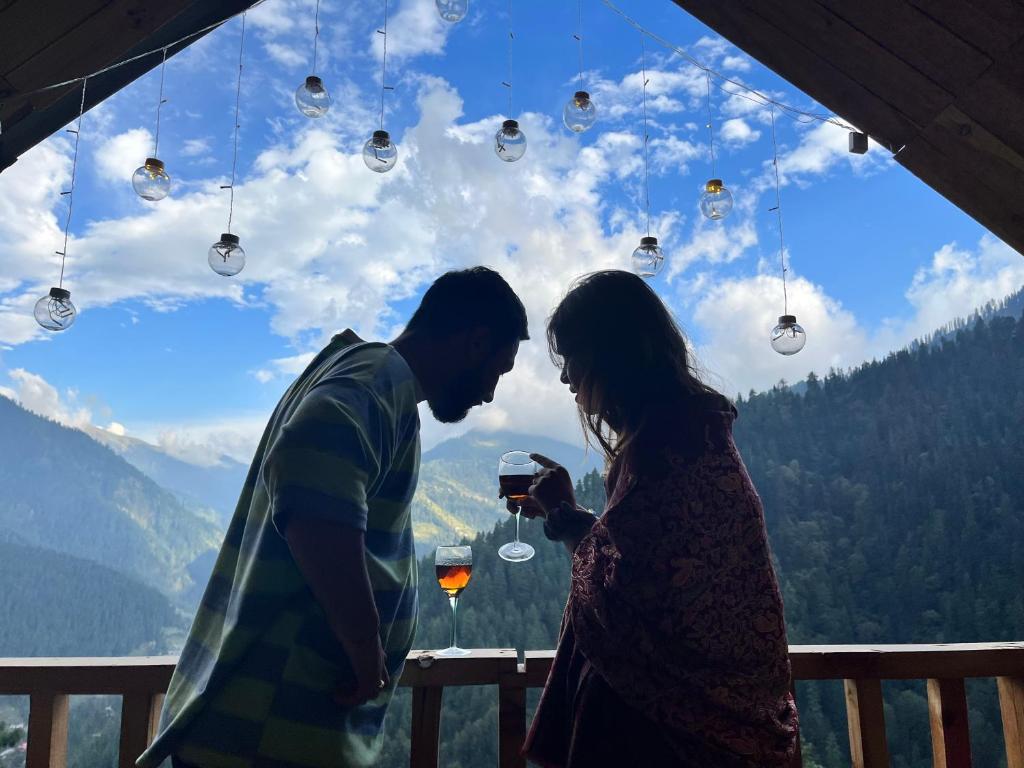 a man and a woman drinking wine in front of a window at Nebula Nook Cottages in Jibhi