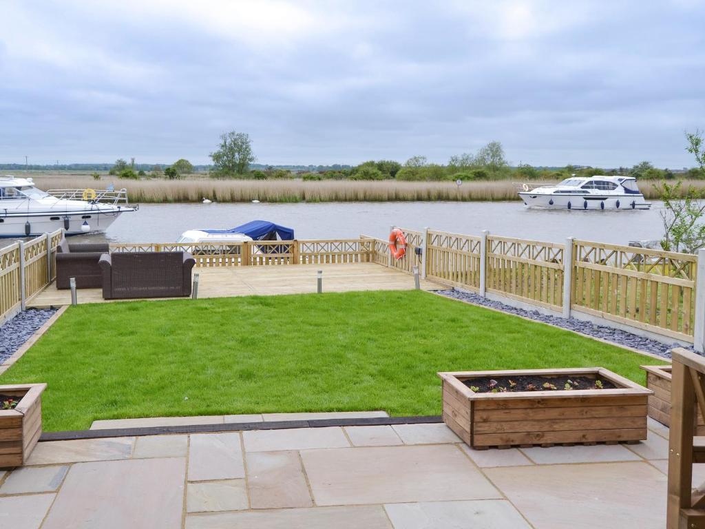 a backyard with a deck with a lawn and boats at Riverbank Cottage in Reedham
