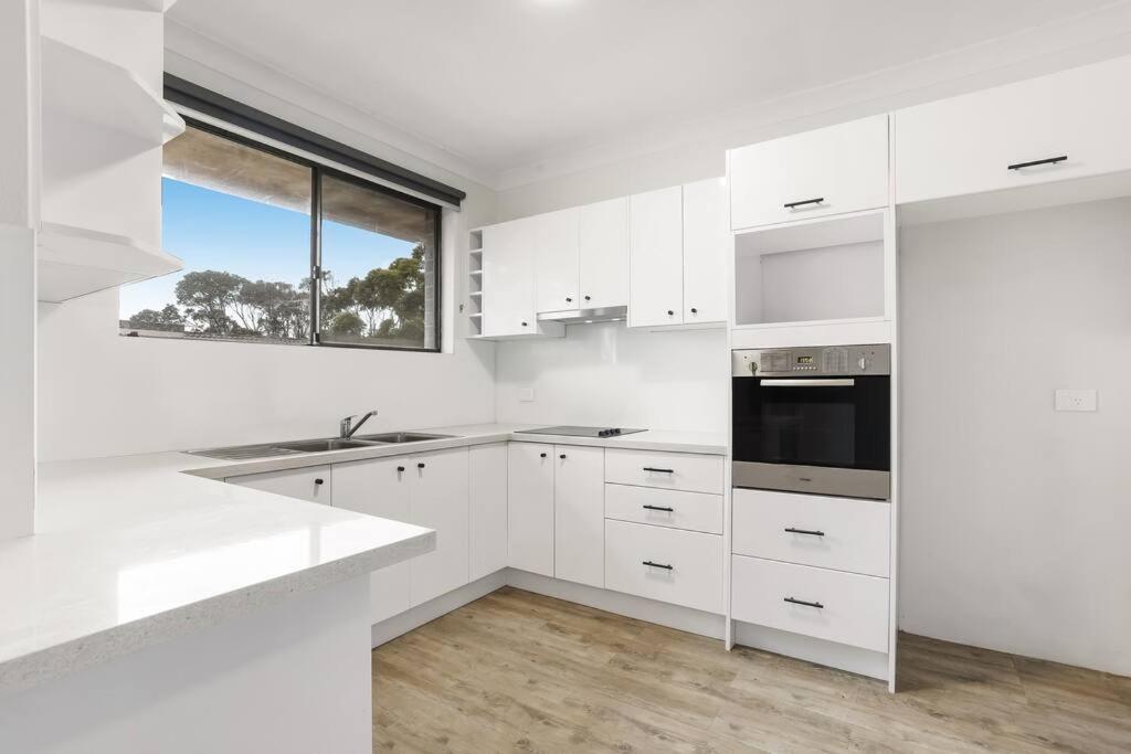 a white kitchen with white cabinets and a window at Central Cronulla Apartment Nestled in the Treetops in Cronulla
